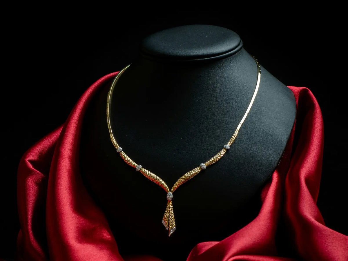 An intricate gold necklace displayed on a dark stand with rich red satin — representing the essence of true luxury where craftsmanship and beauty speak louder than price