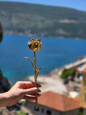 24K gold dipped rose held up against blue sea and coastal hillside view
